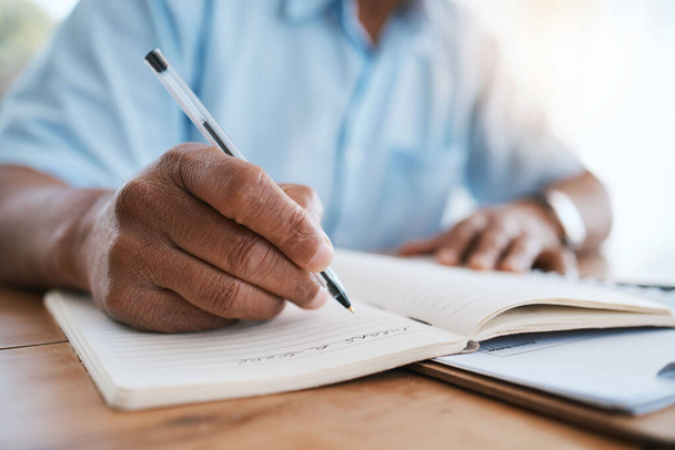 Man, hands and writing in book for finance, budget or schedule planning in remote work at home. Closeup hand of male freelancer taking notes in diary for financial record, expenses or tasks on desk. - Foto, imagen