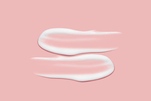 Lots of smears of cosmetic cream. Light, smooth surface. Texture of spreadable cream. Liquid creamy strokes. On a pink background. Cosmetic background, banner. - Photo, Image