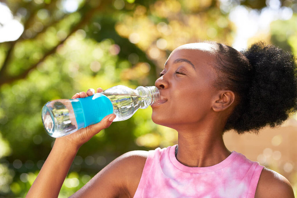 Close up of young Black woman drinking water from glass bottle in park, yoga fun. High quality photo - Φωτογραφία, εικόνα