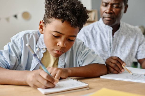 Африканський хлопчик робить нотатки у своєму записнику за столом і робить домашнє завдання з вчителем. - Фото, зображення