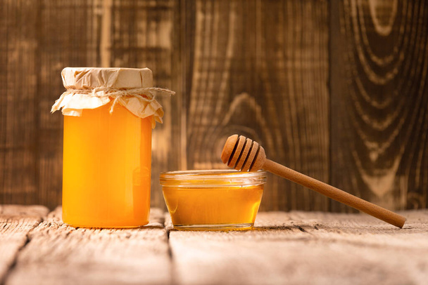 Kreatywny kompozycja miód w szklany słoik i miska, drewniany dysza na postarzały drewniany tło. Koncepcja ekologicznych produktów pszczół. - Zdjęcie, obraz