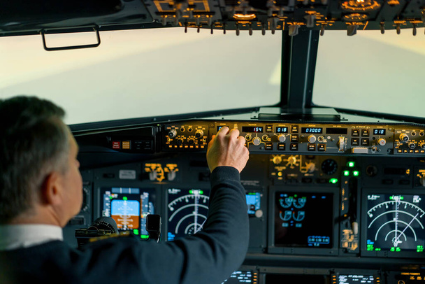 Il pilota preme i pulsanti di accensione sul pannello di controllo per controllare l'aeromobile di fronte al parabrezza della cabina di pilotaggio - Foto, immagini