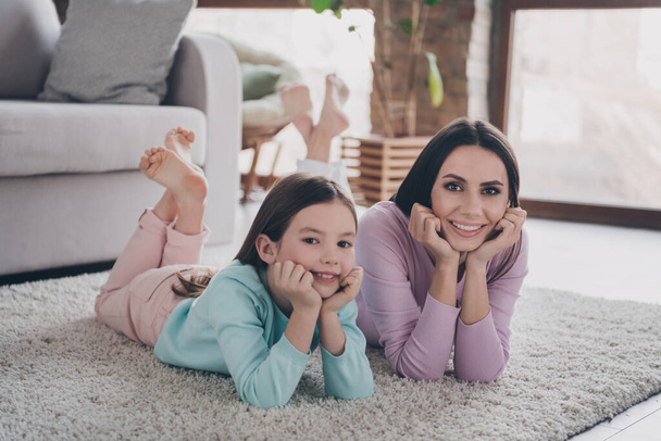 Photo of positive charming family kid girl and mommy lying on floor enjoy free time together modern flat. - Zdjęcie, obraz