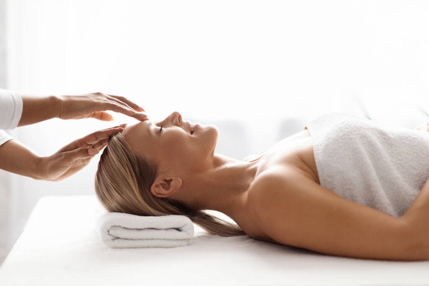 Spa Treatment. Middle Aged Woman Enjoying Relaxing Acupressure Head Massage By Professional Therapist In Beauty Salon, Beautiful Lady Lying On Table With Closed Eyes, Enjoying Wellness Treatments - Foto, imagen