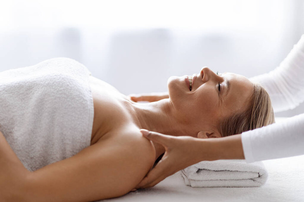 Smiling Middle Aged Woman Getting Wellness Shoulder Massage By Professional Masseur, Calm Mature Female Lying On Table With Closed Eyes, Resting In Luxury Beauty Salon, Side View In Free Space - Photo, Image