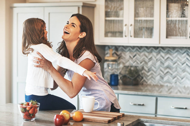 This is why mom needs strong arms. a happy little girl reaching out to hug her mother while sitting on the kitchen counter at home - Foto, Imagen