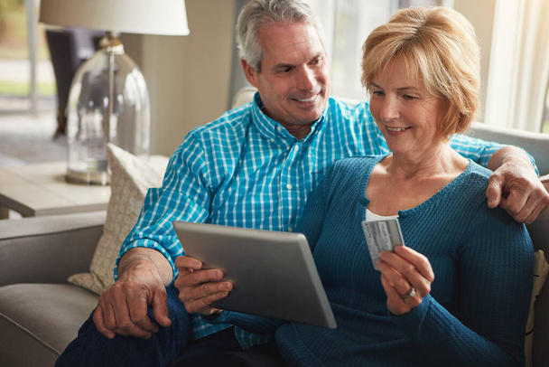 Weve always wanted to book a holiday. Now we can. a happy mature couple relaxing on the sofa and using a digital tablet and credit card together - Photo, Image