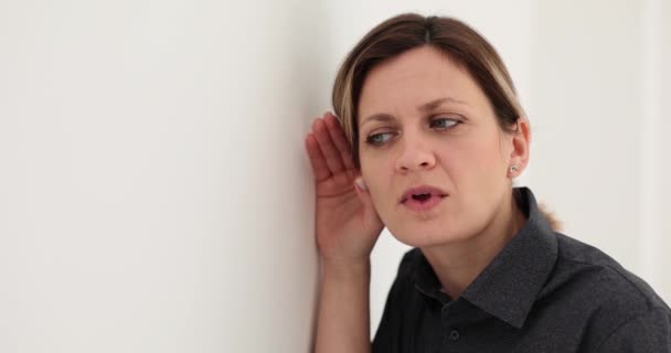 Ciekawa kobieta słucha dyskusji kolegów z pracy. Uważna kobieta z zaskoczonym wyrazem twarzy wkłada ucho w ścianę - Materiał filmowy, wideo