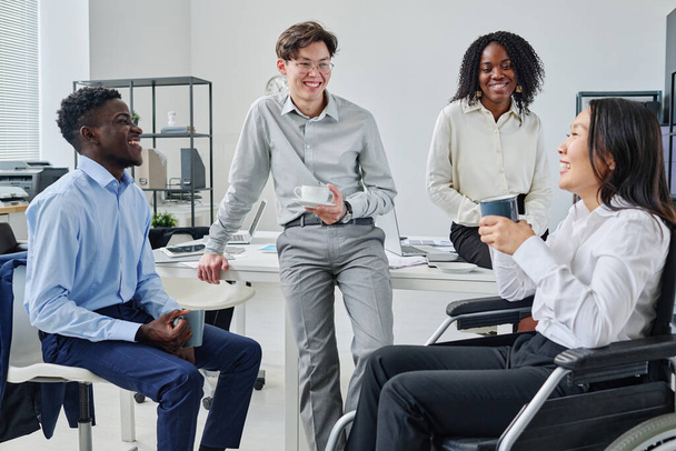 Группа молодых коллег смеется и разговаривает во время кофе-брейка на работе - Фото, изображение