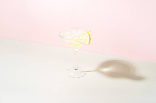 Glazen beker met drank met ijs en limoen tegen roze en groene achtergrond. - Foto, afbeelding
