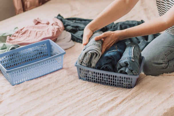 Frau organisiert Kleidung im blauen Container, während sie auf dem Bett sitzt. - Foto, Bild