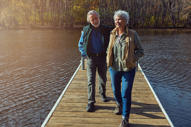 Nie ma lepszego sposobu na emeryturę. para seniorów idąca na spacer na pomoście nad jeziorem - Zdjęcie, obraz