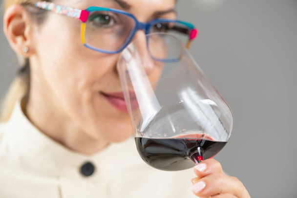 Şarap tatma. Bir kadın kırmızı şarap tatmaktan, şarabın lezzetlerinden ve aromalarından zevk alır.. - Fotoğraf, Görsel