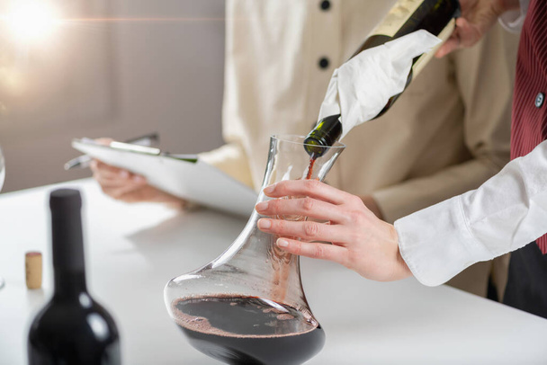 Dekantoimassa viiniä. Sommelier kaataa punaviiniä pullosta dekantteriin ja selittää samalla, miten viiniä ilmastetaan sen maun ja aromin parantamiseksi.. - Valokuva, kuva