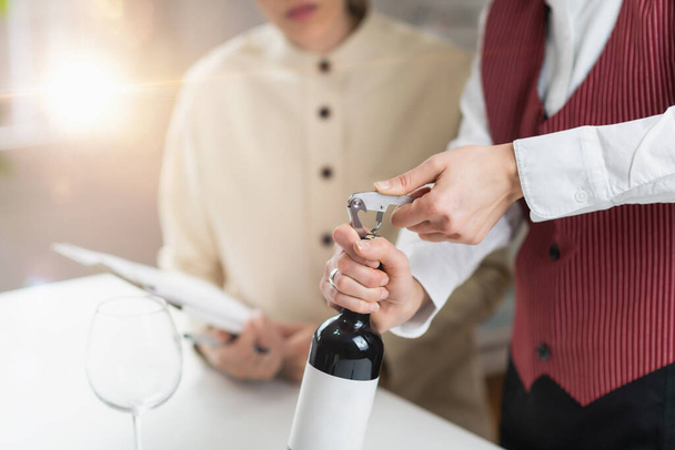 ワインサービスとホスピタリティトレーニング。ソムリエが赤ワインのボトルからコルクを取り除き、ゲストにワインを提供するための適切な技術を示しています. - 写真・画像