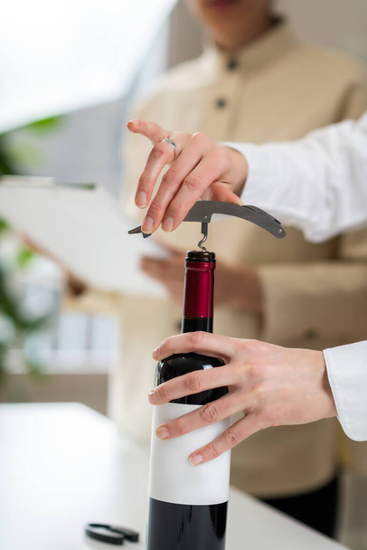 Kurs wychowania do wina. Sommelier pokazuje, jak włożyć korkociąg do korka, co jest podstawową umiejętnością otwierania butelki wina.. - Zdjęcie, obraz