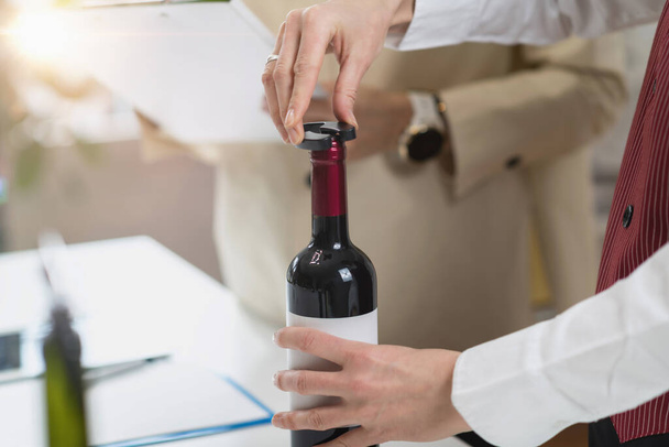 ワインの試飲体験。ソムリエはワインボトルの上面を覆う箔を除去し、サービス用のワインボトルを準備する適切な方法を説明します。. - 写真・画像