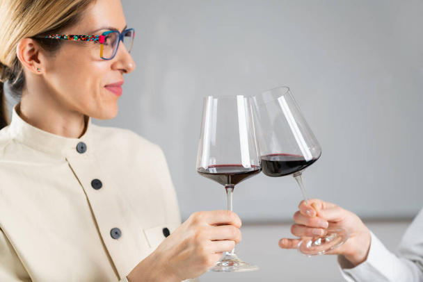 Brindis con vino tinto en un evento de cata de vinos: un brindis femenino con una copa de vino tinto. - Foto, Imagen