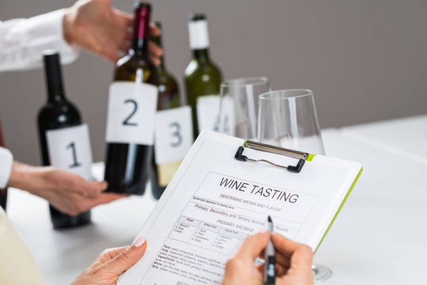 Ik vul een wijnproefformulier in. Wijn proeverij gast evalueert de kenmerken van een rode wijn en vult een wijn proeverij vorm om waarnemingen te registreren. - Foto, afbeelding
