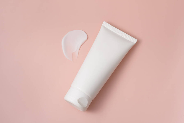 White blank tube of moisturizer or skin lotion with smear on pink isolated background. The concept of cosmetics, presentation or advertising of a new product - Zdjęcie, obraz