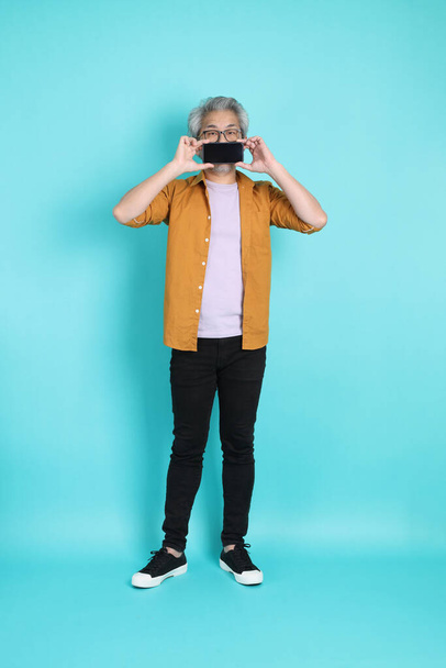 The attractive senior Asian man with yellow shirt standing on the green background. - 写真・画像