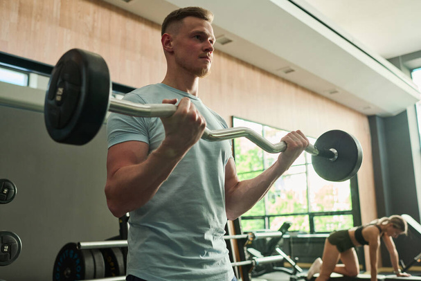 Young man lifting barbell during his sport training in gym - Valokuva, kuva