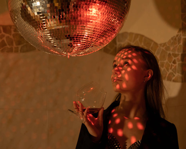 Large portrait of a girl with an empty glass of wine under a shiny ball. High quality photo - Фото, зображення