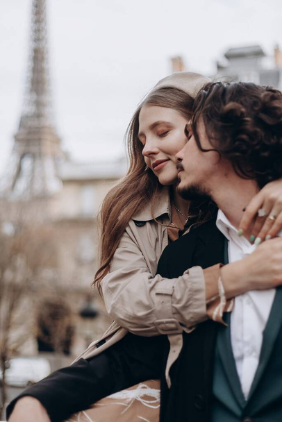 Ένα ερωτευμένο ζευγάρι περπατά στους δρόμους του Παρισιού, ένας τύπος με παλτό και κοστούμι, ένα κορίτσι με φόρεμα με μπερέ και καμπαρντίνα το φθινόπωρο. - Φωτογραφία, εικόνα