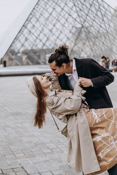 Zamilovaný pár kráčí ulicemi Paříže, muž v kabátě a obleku, dívka v šatech s baretem a pláštěm na podzim - Fotografie, Obrázek