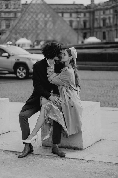 Ein verliebtes Paar spaziert durch die Straßen von Paris, ein Mann in Mantel und Anzug, ein Mädchen in einem Kleid mit Baskenmütze und Trenchcoat im herbstlichen Schwarz-Weiß - Foto, Bild