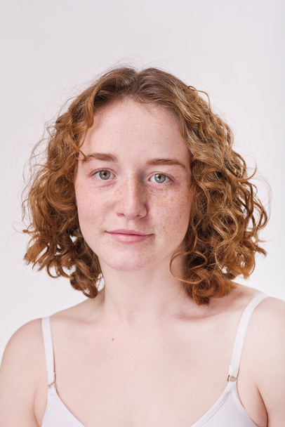 Portrait of red haired girl with curly hair and with freckles on her face looking at camera isolated on white background - Photo, Image