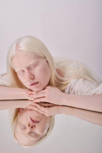 Девушка Альбинос с белыми волосами смотрит в зеркало на белом фоне - Фото, изображение