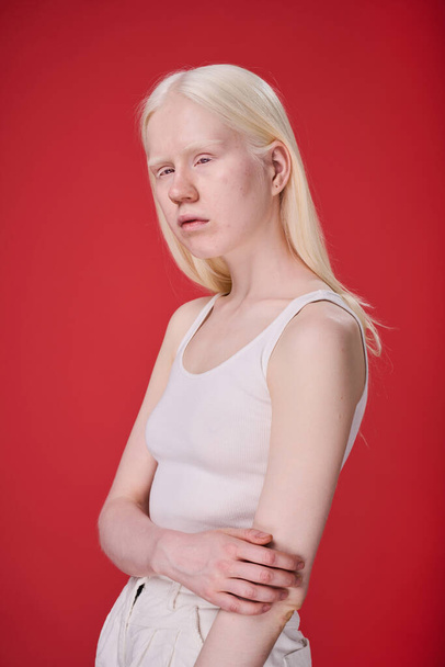 Портрет дівчини-альбіно з незвичайною зовнішністю позує на червоному тлі
 - Фото, зображення