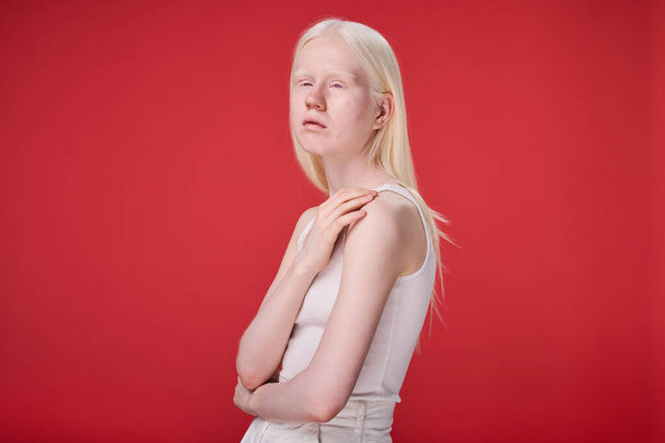 Retrato de menina albina com aparência incomum e beleza natural em pé contra fundo vermelho - Foto, Imagem