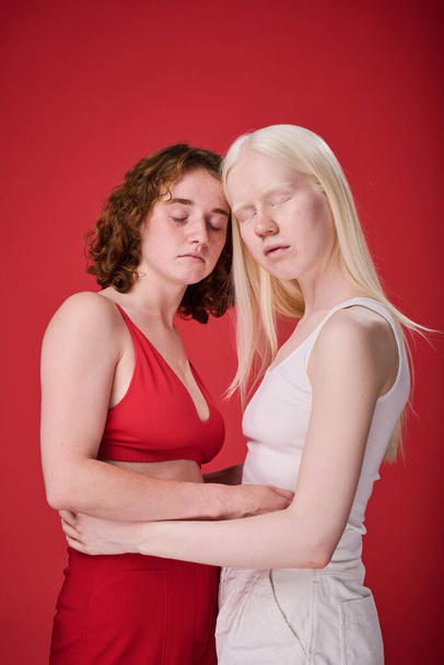 Πορτρέτο δύο κοριτσιών με ασυνήθιστες εμφανίσεις αγκαλιάζει πάνω από το κόκκινο φόντο - Φωτογραφία, εικόνα