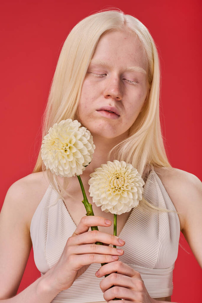 Portrait of young albino girl posing with white flowers against red background - Фото, зображення