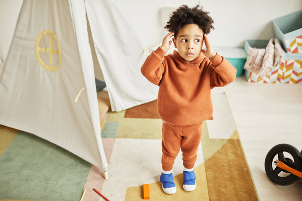 Retrato de cuerpo entero de un lindo niño afroamericano que parece sorprendido y asustado mientras juega en casa y usa un atuendo de moda mínimo, espacio para copiar - Foto, imagen