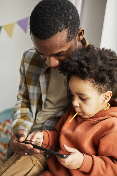 Pystysuora muotokuva musta isä ja söpö pieni poika käyttää älypuhelinta yhdessä ja katsella sarjakuvia verkossa - Valokuva, kuva