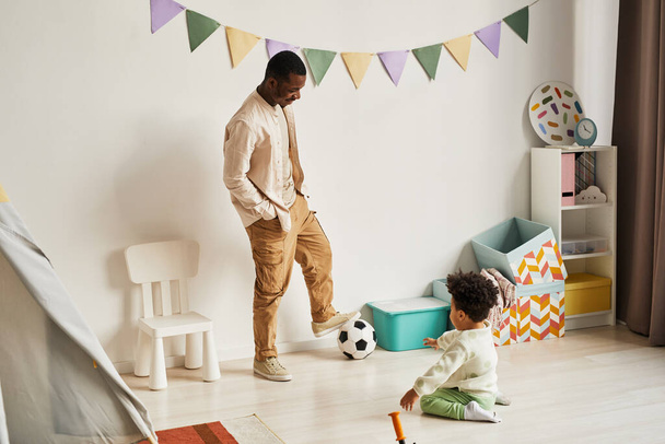 Миниатюрный полнометражный портрет молодого чёрного отца, играющего в футбол с маленьким сыном дома, пространство для копирования - Фото, изображение