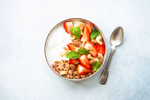 Yogourt au granola et fraises sur blanc. Snack sain ou petit déjeuner, salade de fruits. Vue du dessus. - Photo, image