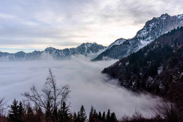 Campogrosso Vicenza Veneto İtalya 'daki dağlık alp ormanları ve küçük dolomitlerin karlı tepeleri arasındaki sis bulutu. - Fotoğraf, Görsel