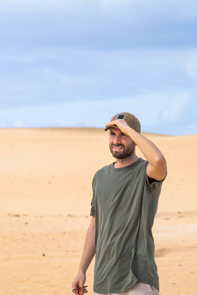 Portrait of loneliness young man with cap looking at the horizon desert dunes at Fuerteventura, Canary Islands - Foto, imagen
