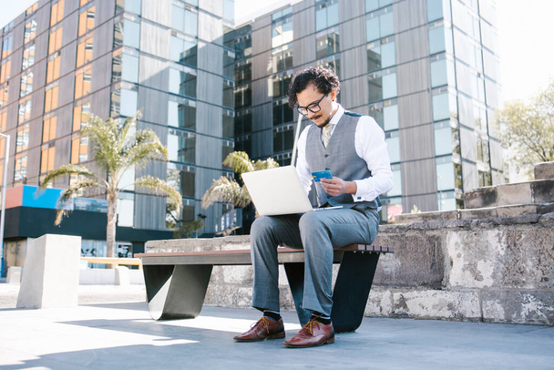 young latin businessman using laptop and holding credit card in Mexico city Latin America, hispanic financial people - 写真・画像