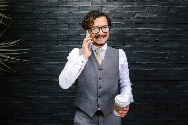 νεαρός Λατίνος επιχειρηματίας που μιλάει από κινητό τηλέφωνο και φοράει κοστούμι στο δρόμο στην πόλη του Μεξικού, ισπανόφωνοι άνθρωποι - Φωτογραφία, εικόνα