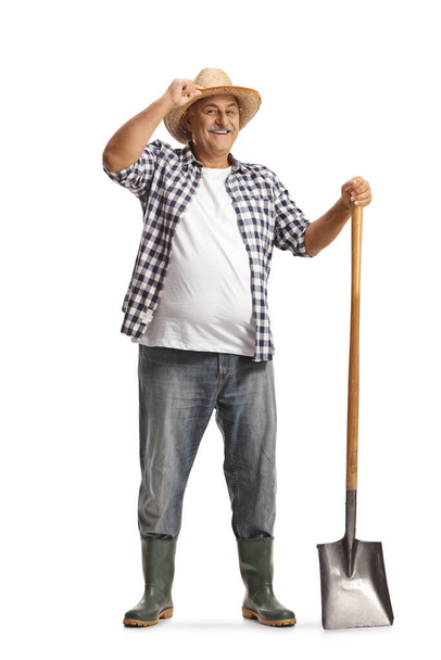 Full length portrait of a happy mature farmer with a shovel greeting with hat isolated on white background - Photo, Image