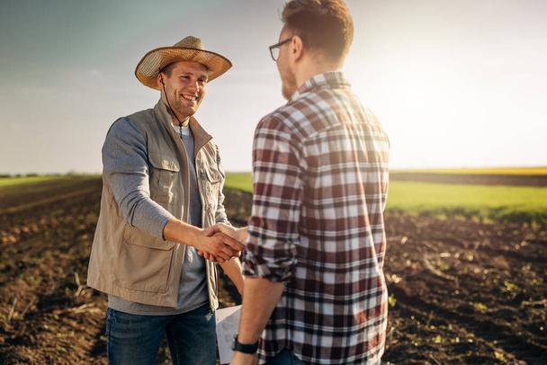 Happy farmer shakes hands with an owner of the farmland he just bought. - Foto, Imagen