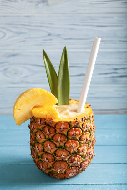 Vertical photo - Pina colada cocktail in pineapple with pineapple slices, straw, two green leaves standing on blue boards - Foto, immagini