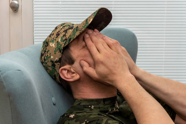 Пожилой человек в военной форме закрыл лицо руками, сидя в кресле. Концепция: психические расстройства у военнослужащих, лечение психотерапевтом. - Фото, изображение
