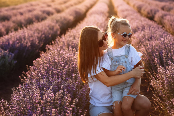 Happy family in purple lavender field. young beautiful mother and child Girl enjoy walking blooming meadow on summer day. Mom having fun with pretty daughter in nature on sunset. mothers day. - 写真・画像