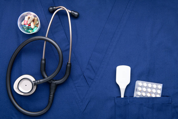 stethoscope with pills and thermometer is lying on a blue medical gown. View from above. Space for text. - Foto, immagini